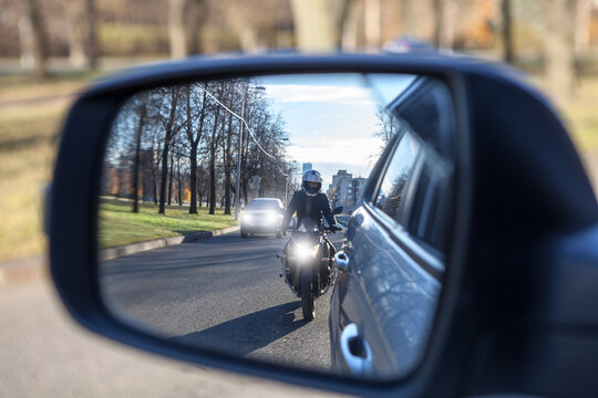 Mutual passing, motorcycle and vehicle with dazzle lighting overtaking the car, view in a side mirror. Improper driving or traffic violation