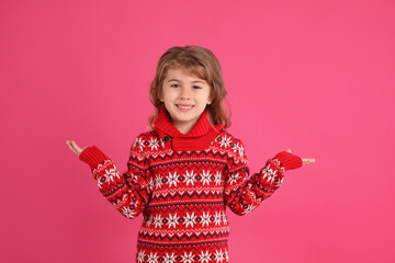 Cute little girl in red Christmas sweater smiling against pink background