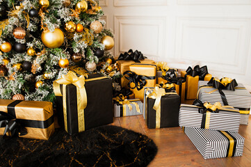 lots of gift boxes in wrapping paper and ribbons in black and gold colors under big fluffy Christmas tree with garland, Christmas card, selective focus