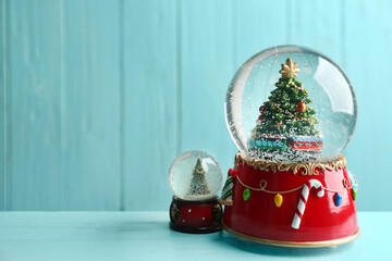 Beautiful snow globes with Christmas trees on light blue wooden table, space for text