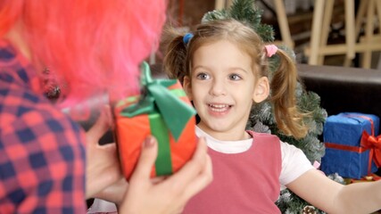 Modern mom with red hair gives a gift box to her little smiling daughter. Three-year-old beautiful girl laughs and rejoices at the Christmas or New Year gift. Positive emotions, happy child. 