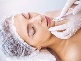 Beautician doing beauty procedure with syringe to face of young brunette woman in sunny spa center. Cosmetic medicine and surgery, beauty injections