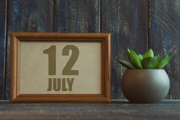 july 12th. Day 12 of month, date in frame next to succulent on wooden background summer month, day of the year concept