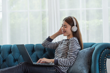 Young Asian woman enjoy listening to music with headphones and using laptop, happy and relaxing time