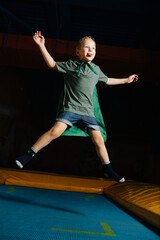 Confident boy in a cape jumping on trampoline in entertainment center