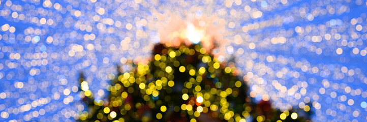 Obraz premium bokeh or blurred glow lights of glowing garlands on a decorated Christmas tree against the sky view from below. banner