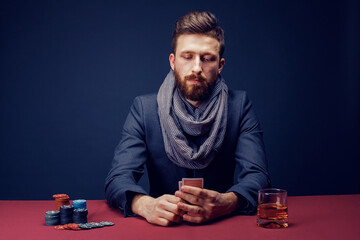 Stylish bearded Man in suit and scarf playing in dark casino, smoking cigar, drink whiskey.