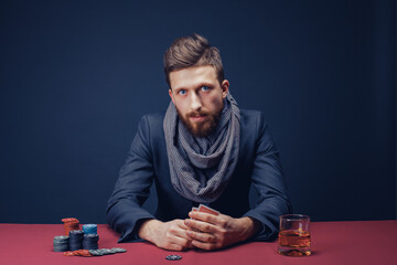 Stylish bearded Man in suit and scarf playing in dark casino, smoking cigar, drink whiskey.