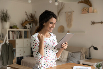 Overjoyed millennial female look at pad screen feel euphoric win online lottery on gadget. Happy...