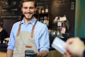 Customer using credit card for payment to owner at cafe restaurant, cashless technology.