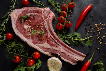 Fresh Raw Beef bone rib steak on black board with herbs and spices