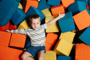 Casual little boy in a multi-color soft cube pool in entertainment center