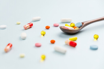 Various colorful multicolored pills on blue background. Tablets in a wooden spoon. Medicines, vitamins, antibiotics and medicaments. First aid treatment and healthcare concept. Selective focus.