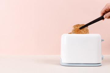 Black tongs take out the bread out of the white toaster. Levitation food. Delicious breakfast concept. Pink background. Copy space. Flat lay, side view. Kitchen equipment for fresh morning meal.