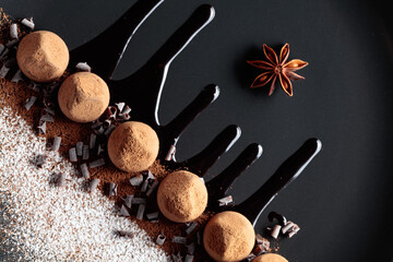 Chocolate truffles on a black plate with chocolate sauce.