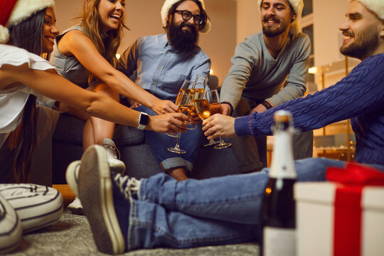Group of friends sitting on floor and clinking glasses of champagne during Christmas holiday festive party