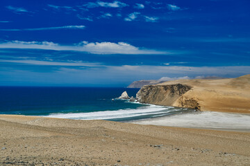 desolate and vast landscape of Paracas at the coastline of Peru, a place were desert meets the ocean. Showing blue sky, clouds and a sandy desert beach