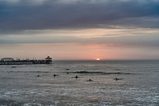 Playa Varadero, Huanchaco, at sunset over the pacific ocean with some surfers in the water and the long jetty in the background