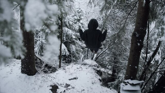 a woman in a black down jacket in the snow swings on a swing alone. an image of loneliness and solitude.