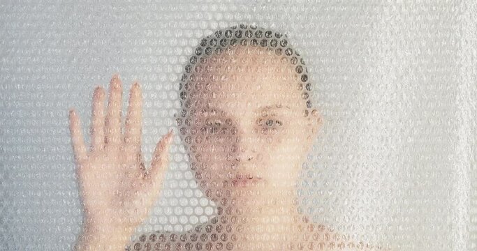 Covid-19 lockdown. Self isolation crisis. Quarantine measures. Depressed sad woman suffering alone behind plastic bubble wrap transparent protective wall.