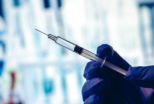 Vaccine - injection of a vaccine with a syringe - solution against the Covid-19 coronavirus - close-up on a syringe and a hand with a blue glove - Laboratory background
