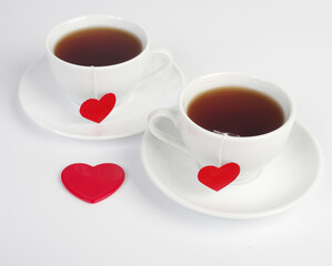 Two white cups of tea with red hearts in the form of labels on a white background.Tea for two.