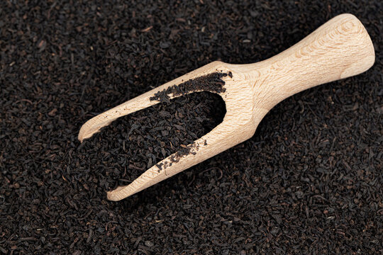 Dry black tea leaves on which there is a wooden scoop for a set of bulk products.