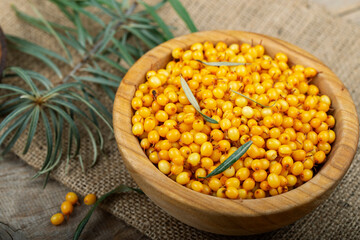 Sea buckthorn with leaves in a wooden bowl on a wooden table.