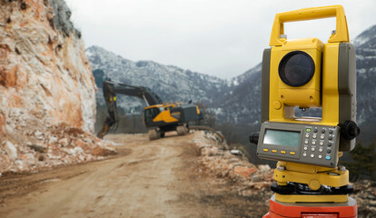 Theodolite (total positioning station) on a background of road construction in mountains - obrazy, fototapety, plakaty