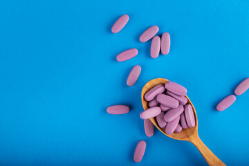 Pills in a wooden spoon on a blue background. Health care concept. Space for text. Conservative medicine.
