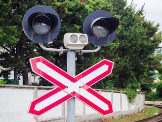 A double unlit traffic light with red white arrows in a cross stands at a railway crossing