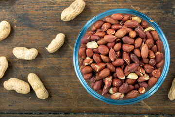 Peanuts in their husks in a glass bowl and peanuts in their skins are scattered on the table. Space for text.