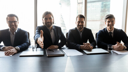 Wide banner panoramic view of smiling male employers sit at desk stretch hand meet new employee into team. Happy successful businessmen welcome newcomer or newbie. Success, employment concept.