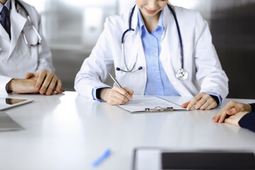 Unknown woman-doctor with male colleague are consulting patient woman while sitting at the desk in modern clinic, close-up. Perfect medical service, medicine during Coronavirus pandemic. Covid 2019