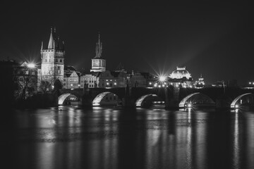 Fototapeta premium Evening panorama of Prague, Czech Republic. Black and white photo. Charles Bridge,Karluv most reflected in Vltava River. Long exposure city lights.Amazing European cityscape.Travel urban concept.