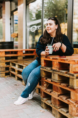 Portrait of a young adult girl with a Cup of coffee near a cafe in good autumn weather