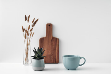 A mug, a potted houseplant, a clear vase and a wooden cutting board. Eco-friendly materials in the decor of the room, minimalism. Copy space, mock up