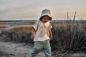 Two-year-old child in a hat walks along a country road, summer. Knowledge of the world.