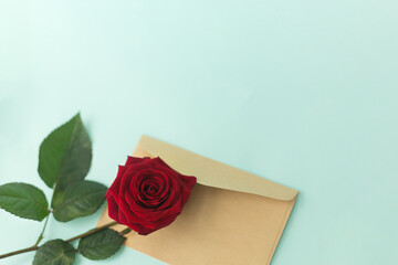 Red rose and envelope on a light green background. Minimalist concept for your mockup and project. Layout, flat lay, copy space, top view. Selective focus.