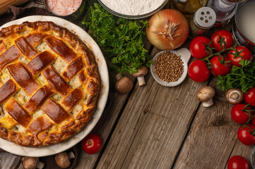 Ruddy meat pie on wooden table with variety of ingredients background. Concept of cooking process. Backstage of preparing tasty meal. View from above. Flat lay. Recipe book. Space for text.
