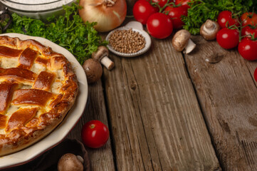 Ruddy meat pie on wooden table with variety of ingredients background. Concept of cooking process. Backstage of preparing tasty meal. Flat lay. Recipe book. Space for text. Horizontal format.