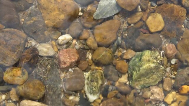 pebble or gravel and round stone beach in stream or flow river and shallow pond with sea to clear transparent by clean water wave on top view or foot spa and nature massage and for texture background