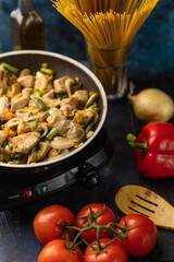 Pan with fragrant frying meat on marble dark blue table with variety of ingredients background. Backstage of cooking spaghetti pasta. Concept of cooking process. Cookbook design. Vertical format.