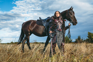 Knight woman in armor with a horse against the sunset fields background