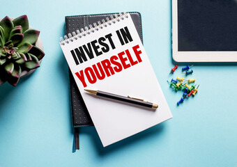 On a light blue background, there is a potted plant, a tablet and a weekly with the text INVEST IN YOURSELF