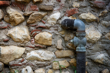 Detail of a gas pipe outside a house with a stone wall.