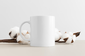 White mug mockup with a cotton branch on a beige table.
