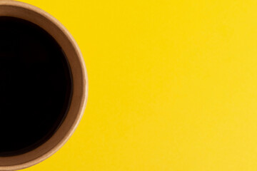 Black coffee in disposable paper cup on yellow background. Top view, close-up.