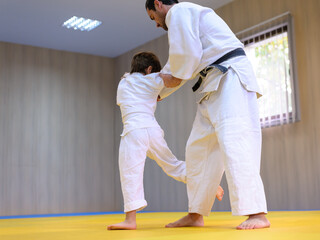 Young white belt judo kid practicing leg throw with his judo teacher