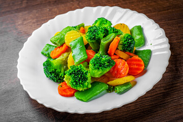 Mixed vegetables. green bean, broccoli and carrots in white plate on a wooden table background.
